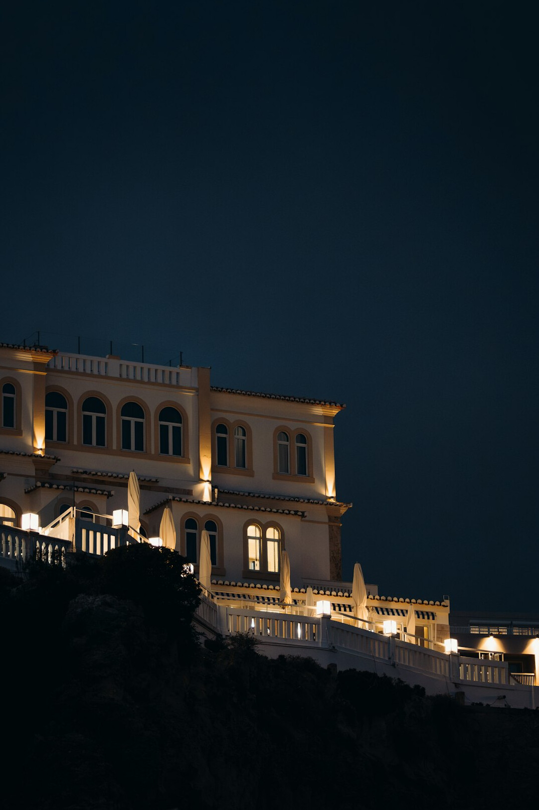 Exterior of a grand hillside mansion at dusk with warm lights